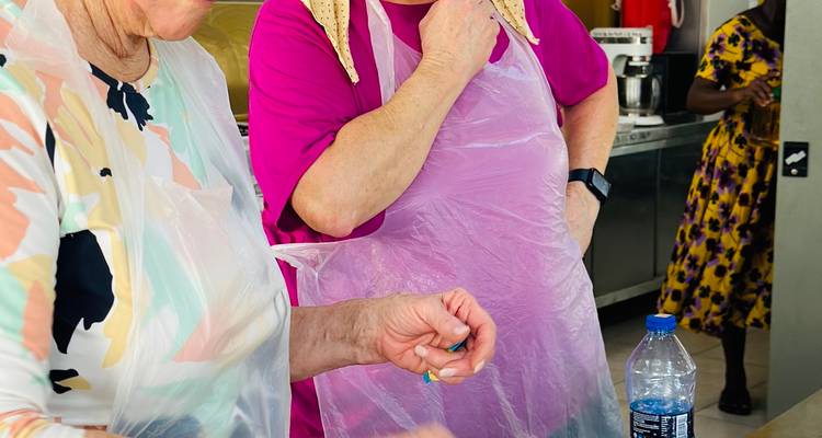 Teilnehmer mit Schürzen lernen Kochtechniken in einem hell beleuchteten Küchenklassenzimmer.