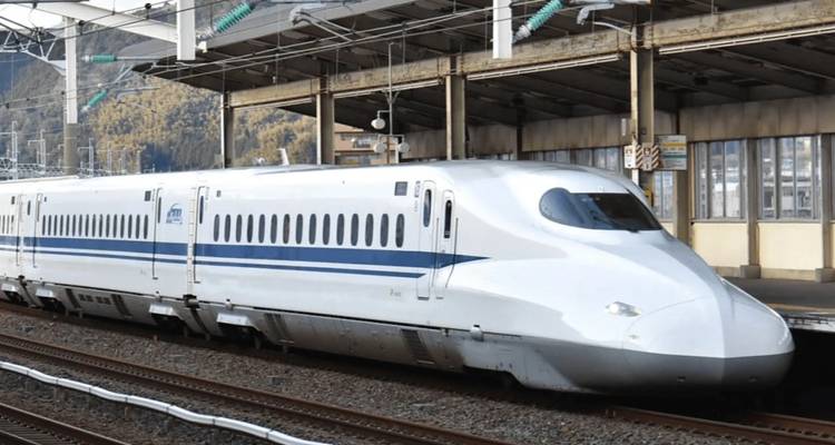 Hochgeschwindigkeitszug an einem Bahnhof mit Bergen im Hintergrund.