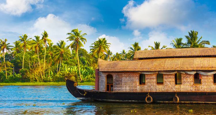 Traditionelles Hausboot auf einer ruhigen Wasserstraße mit üppigem Grün und Palmen im Hintergrund.