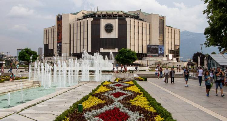 Plaza con fuentes y gente caminando alrededor.