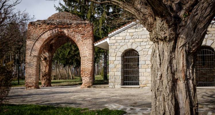 Arco de ladrillo y un edificio de piedra entre los árboles.