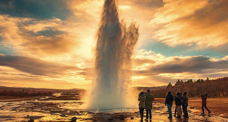 Geyser erupting at sunset with onlookers around.