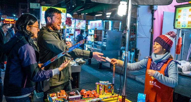 Des gens qui interagissent à un stand de nourriture dans un marché de nuit.