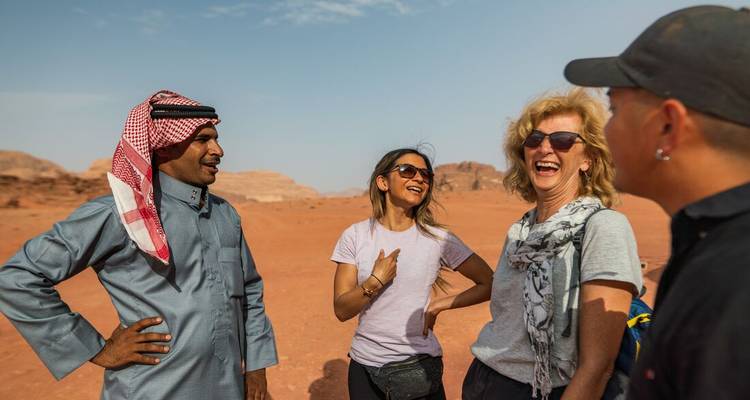 Un guide vêtu du keffiyeh traditionnel discute et rit avec trois voyageurs dans le désert aux sables rouges de Wadi Rum.