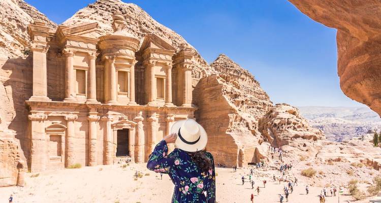 Le voyageur coiffé d'un chapeau de soleil contemple la façade monumentale du Monastère taillée dans les falaises rose-rouge de Pétra.