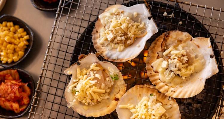 Coquilles Saint-Jacques grillées au fromage sur un grill chaud accompagnées de plats d'accompagnement.
