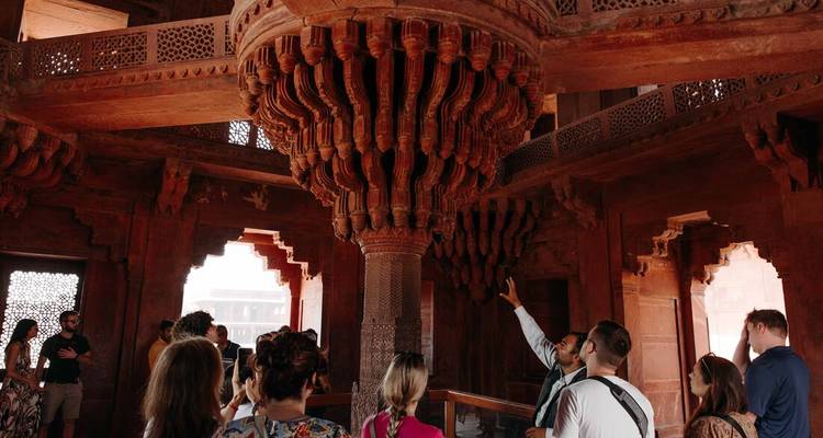 Guided tour inside intricately carved sandstone hall with central ornate pillar at Fatehpur Sikri