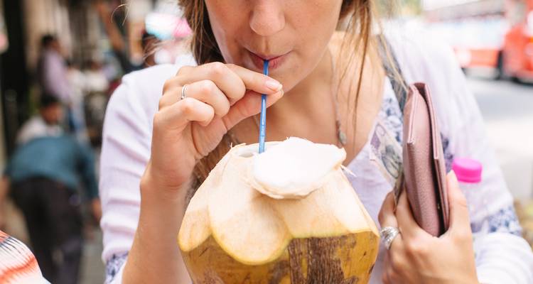 Person drinking from a coconut with a straw in a street market.