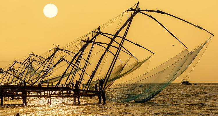 Silhouette of fishing nets against a sunset sky over water.