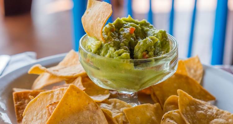 Bowl of guacamole with tortilla chips on a plate.