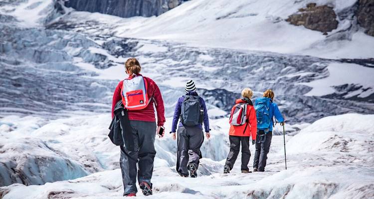 Des gens qui font de la randonnée sur un glacier avec des montagnes enneigées en arrière-plan.