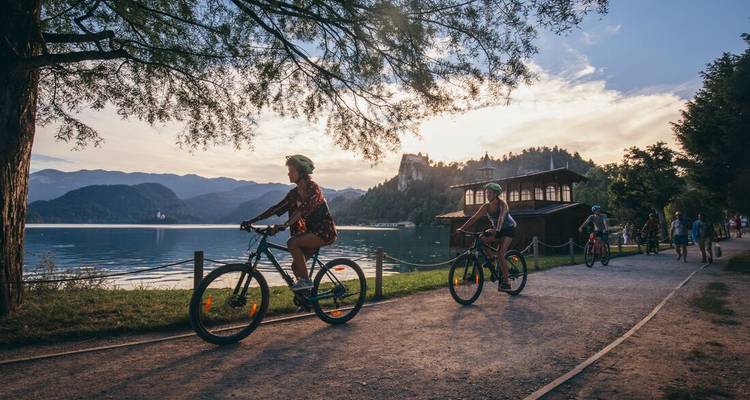 People cycling along a lakeside path with mountains in the background.