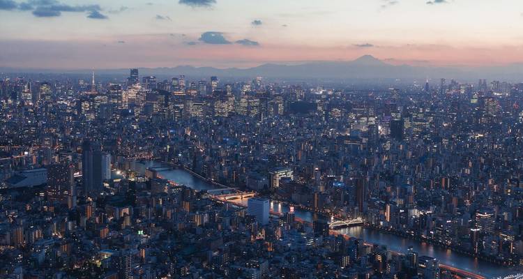 Een uitgestrekt schemerlandschap van Tokyos skyline met lichtstromen en Mount Fuji in de verte aan de horizon.