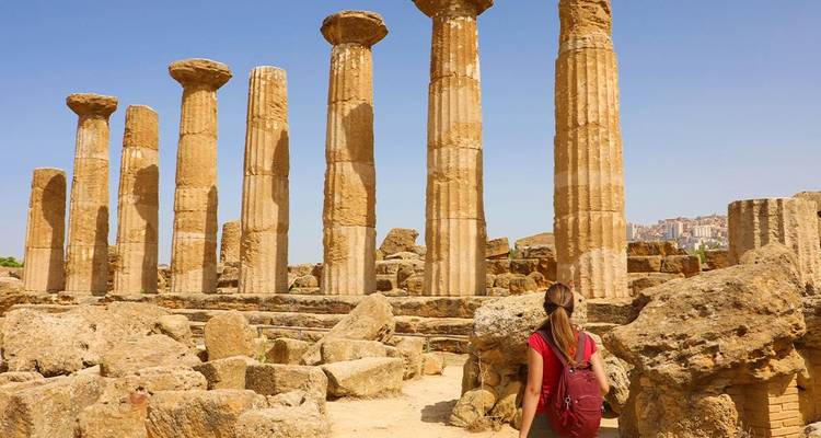 Viajero con mochila explora imponentes columnas griegas antiguas entre ruinas bañadas por el sol en el Valle de los Templos.