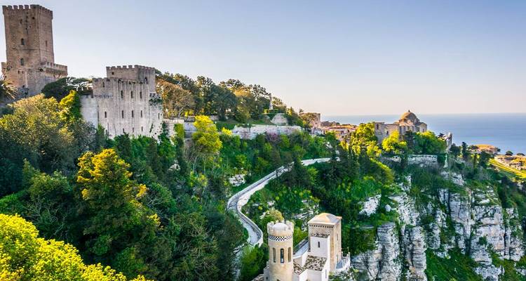 Castillos de piedra medievales y frondosos árboles coronan un acantilado dramático con vista al resplandeciente Mar Mediterráneo.