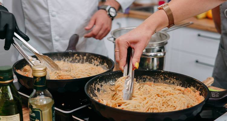 Primer plano de manos mezclando pasta cremosa en sartenes durante una clase de cocina siciliana.