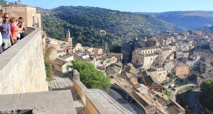 Los turistas se asoman por encima de una balaustrada de piedra hacia las pintorescas casas escalonadas que se extienden por el valle de Ragusa.