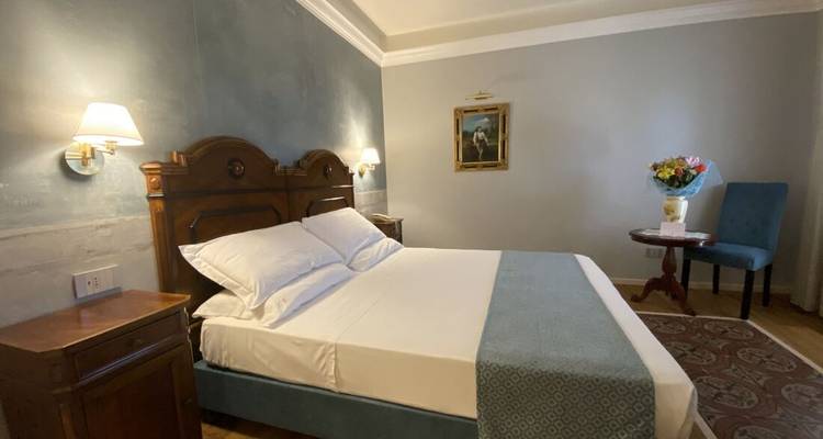 Habitación de hotel siciliano tradicional con cabecero de madera, iluminación suave y decoración clásica.