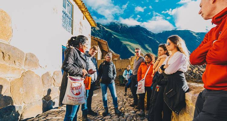 Reiseführer spricht mit Reisenden, die auf gepflasterter Straße neben rustikalem Andenhaus im Dorf Ollantaytambo stehen.