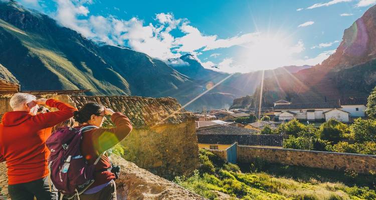 Reisepaar fotografiert Sonnenaufgang über Talstadt, eingerahmt von hoch aufragenden Andengipfeln.