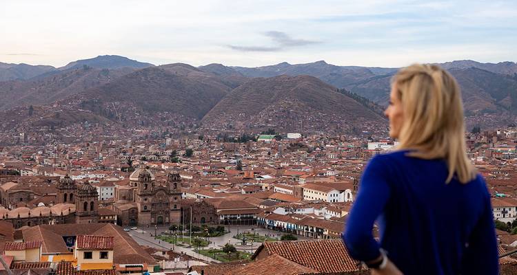 Frau blickt über Terrakotta-Dächer des weitläufigen Cusco-Beckens zu den umliegenden braunen Bergen.
