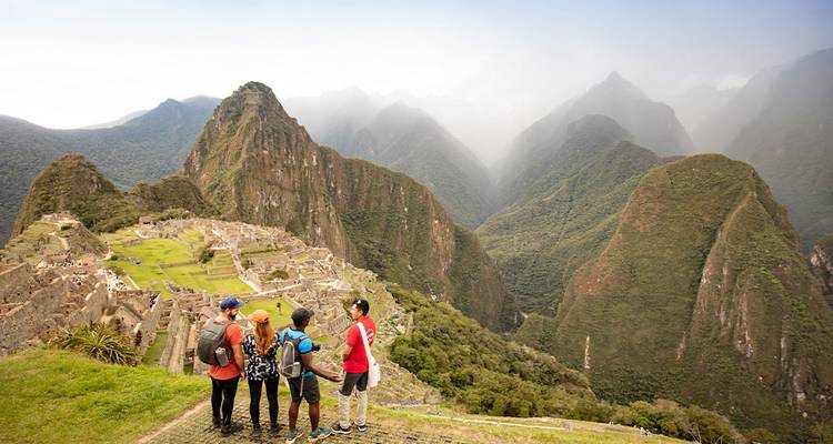 Gruppe von Wanderern bewundert nebelverhangene Gipfel und alte Steinterrassen von Machu Picchu vom klassischen Aussichtspunkt aus.