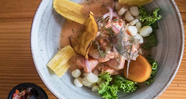 Gourmet-Schüssel mit peruanischem Ceviche, garniert mit Riesenmais, Kochbananenchips und frischem Grün auf Holztisch.