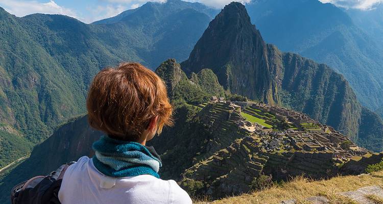 Reisender in Schal gehüllt bewundert weitläufige Aussicht auf Machu Picchu Ruinen, eingebettet zwischen steilen grünen Gipfeln.