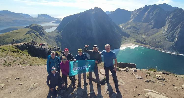 Grupo de senderismo sosteniendo una bandera de Exodus en la cima de una cresta montañosa con vistas a fiordos y picos espectaculares.