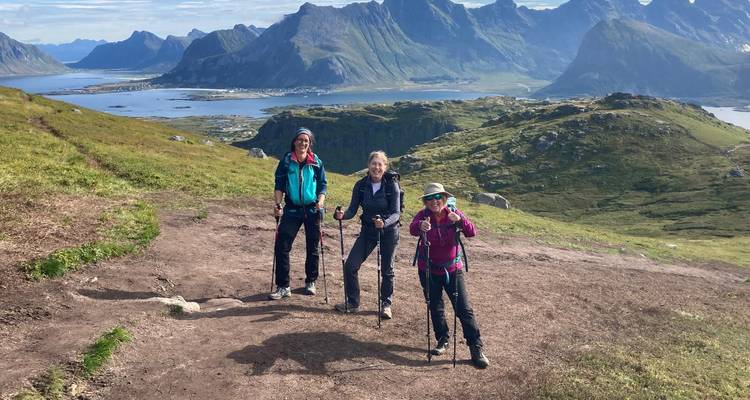 Tres trekistas posan en un sendero de montaña con los picos escarpados de Lofoten y agua abajo.
