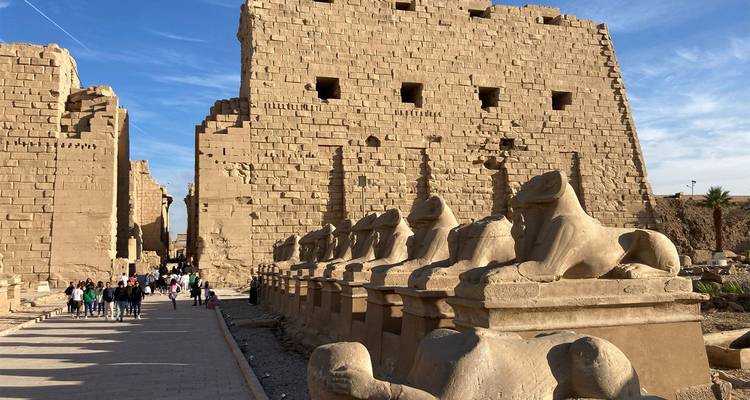 Bezoekers wandelen langs sfinxbeelden buiten de imposante zandstenen muren van de Karnak-tempel.