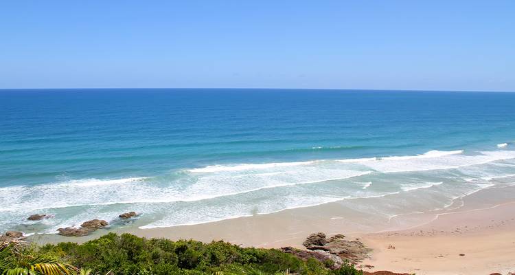 Hoher Aussichtspunkt über weiten leeren Strand und türkisfarbene Atlantikwellen unter klarem Himmel.