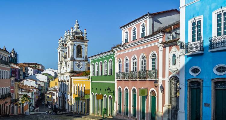 Fachadas coloniales coloridas y torre de iglesia barroca en una calle empedrada del distrito Pelourinho de Salvador.