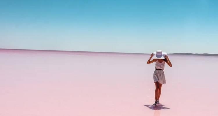 Personne marchant sur un lac aux eaux roses sous un ciel bleu clair.