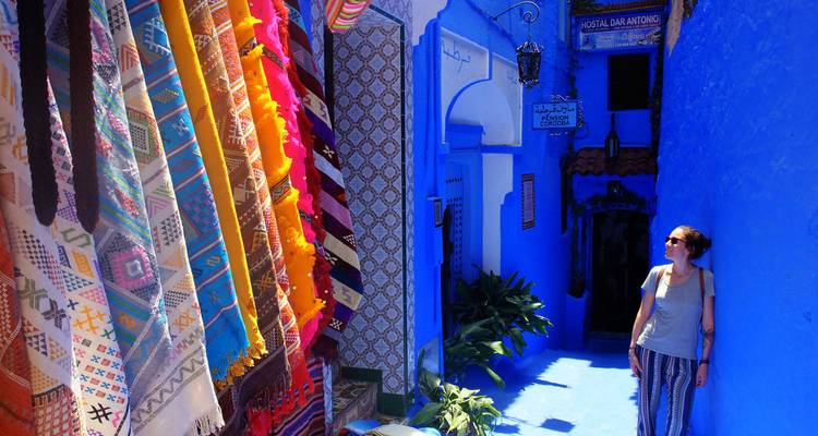 Des textiles colorés suspendus dans une rue d'une ville aux murs bleus.
