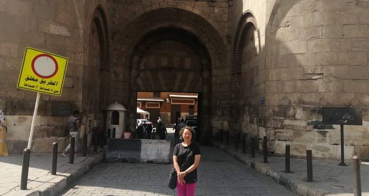 Vrouw poserend bij een historische stenen poort in een stad.