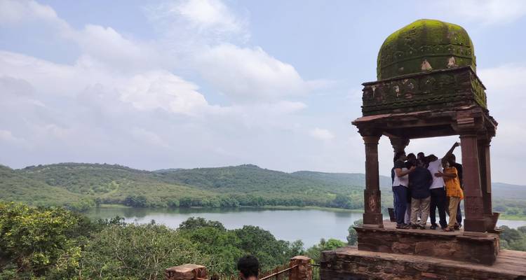 Group of people standing under a pavilion with a lake view.