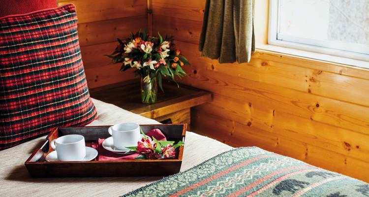 Nahaufnahme eines gemütlichen Hütten-Schlafzimmers mit Tassen und Blumen auf einem Tablett.