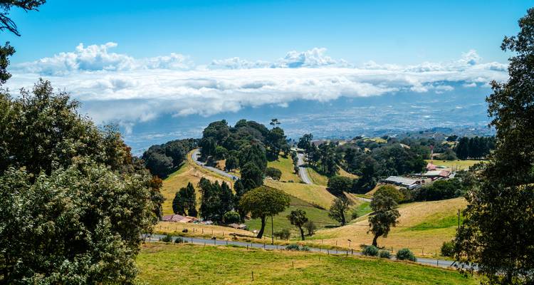 Panoramablick auf ein Tal mit einer gewundenen Straße, über den Wolken.