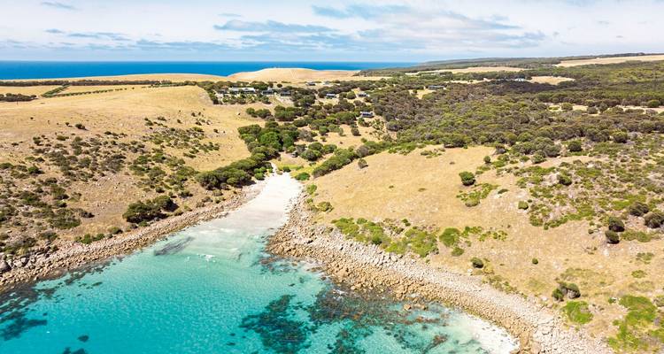 Luchtfoto van een strand met turquoise water en omliggende heuvels.