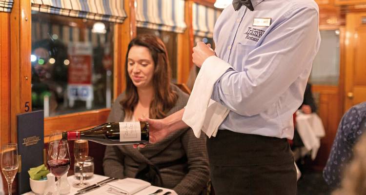 Waiter serving wine in a train dining car with passengers.
