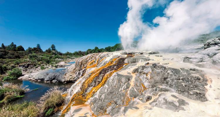 Geothermal area with steaming vents and colored rocks.