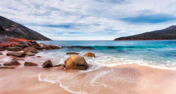 Beach with soft sand, large rocks, and clear turquoise water.