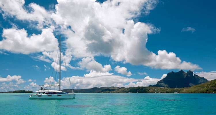 Sailboat on clear turquoise water with mountains in the background.