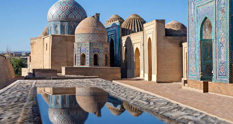 Historisch mausoleum complex met ingewikkeld tegelwerk en koepels die reflecteren in het water.