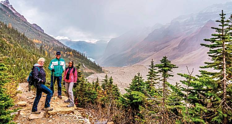 A group of hikers standing on a mountain trail with misty mountains in the background.