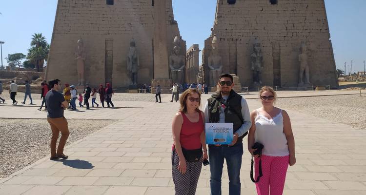 Drie toeristen die poseren voor grote oude standbeelden en een pyloon.