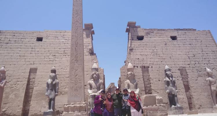 Vier toeristen die voor een grote obelisk en oude beelden staan.