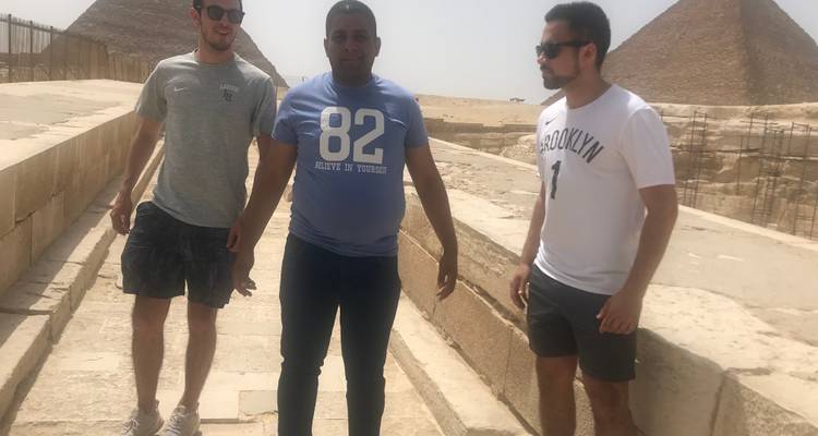 Drie mannen die op een loopbrug staan met de piramides op de achtergrond.