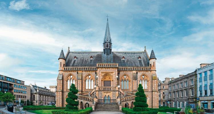 A historic building with intricate Gothic architecture and a pointed spire, set against a blue sky.